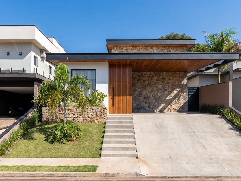 Fachada frontal da residência de alto padrão, com revestimento em pedra e madeira